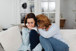 young woman supporting crying female friend on couch
